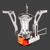 A very small, silver and orange camping stove with foldable pot supports extended is shown next to its bright orange plastic carrying case against a stark white background. The stove has a small red lever for controlling the gas flow and a visible piezo igniter.
