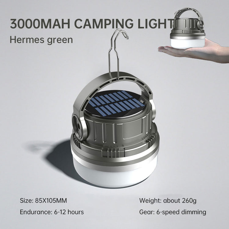 A round, silver and white camping lantern with a black solar panel on top and a silver hanging hook extended. Text above the lantern reads "3000MAH CAMPING LIGHT" and "Hermes green". Smaller text below indicates size, endurance, weight, and dimming modes. A hand holding a smaller version of the same lantern is visible in the upper right corner.