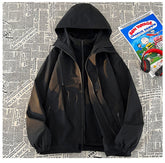 A black 3-in-1 mountain assault suit with a hood and a partially visible inner layer, laid out against a background of newspaper print.