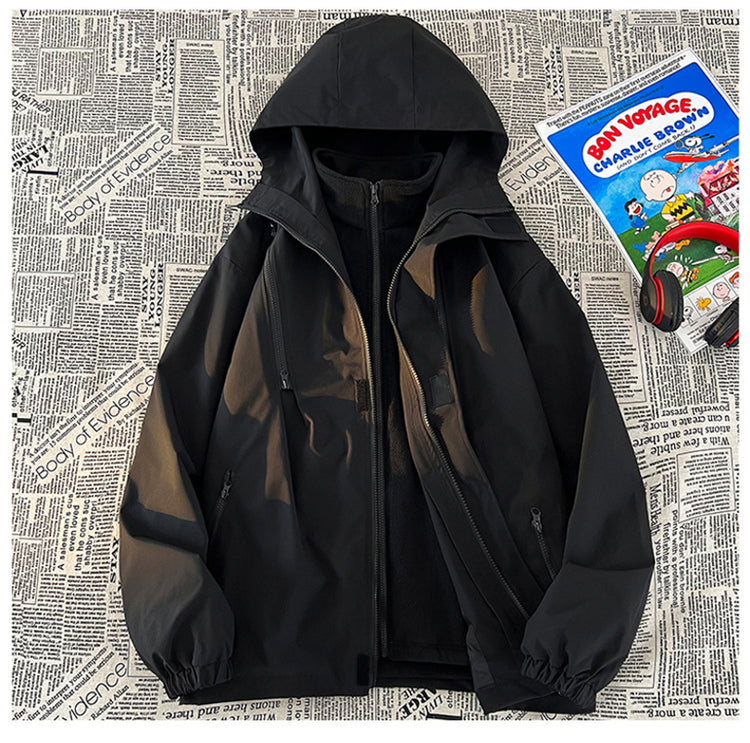 A black 3-in-1 mountain assault suit with a hood and a partially visible inner layer, laid out against a background of newspaper print.