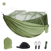 An olive green outdoor camping hammock with a fine white mosquito net suspended above it. Below are a matching olive green storage bag, two black tree straps, two black carabiners, and a bundle of green rope. A small olive green circle is in the upper left corner.