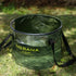 A translucent army green Nobana 30L folding bucket filled with water sits on green grass. The bucket has black trim and black carrying straps. The Nobana logo and "30L BUCKET Enjoy the beauty of nature" are printed in yellow on the side.