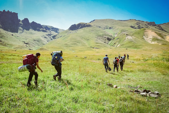 people walking on green field near mountains