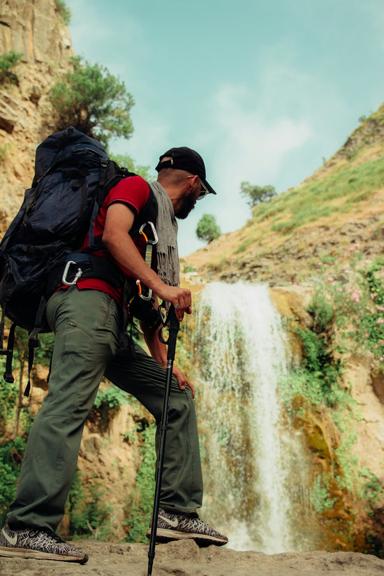 Hiker stands near a waterfall with a large backpack.