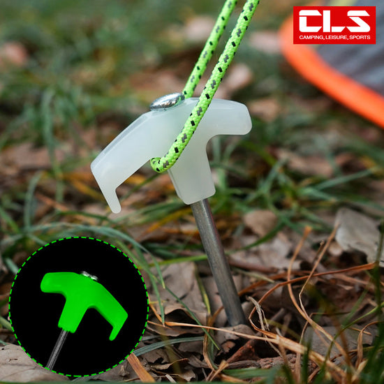 A single 25cm steel tent peg with a bright green, glow-in-the-dark plastic head, securely inserted into the ground with a green guyline attached, illustrating its use for visible and stable tent anchoring during outdoor camping.