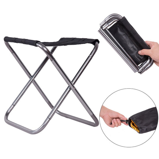 A small, lightweight folding stool with a silver aluminum frame and a black fabric seat is shown in its open position next to a hand holding the same stool in its folded, compact form.