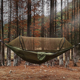 An olive green camping hammock with a black mosquito net extended above it is shown. Below the hammock are two silver carabiner clips attached to black straps, a coiled black tree strap, and an olive green stuff sack.