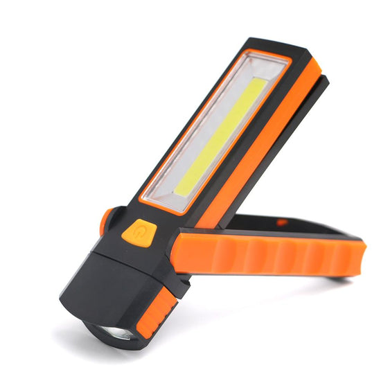 An orange and black COB LED work light is shown angled slightly to the left against a white background. The light features a rectangular COB LED panel, a smaller round LED at the top, an orange foldable base that can act as a stand, a magnetic base, and a hook. An orange power button is visible on the side.