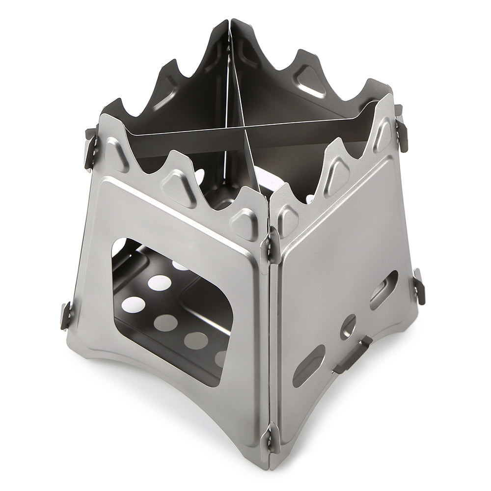 A small, silver stainless steel wood-burning stove is shown unfolded against a white background. The stove has a boxy structure with air vents and a cross-shaped trivet on top.
