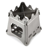 A small, silver stainless steel wood-burning stove is shown unfolded against a white background. The stove has a boxy structure with air vents and a cross-shaped trivet on top.