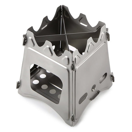 A small, silver stainless steel wood-burning stove is shown unfolded against a white background. The stove has a boxy structure with air vents and a cross-shaped trivet on top.