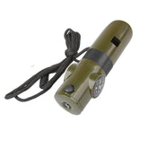 An olive green, cylindrical 7-in-1 survival whistle kit is shown diagonally against a white background. The kit has a black lanyard attached to one end. Visible features include a whistle opening, a button for the LED light, a small compass on the side, and a black ridged grip.