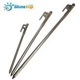 Three silver ShineTrip tent pegs of varying lengths and thicknesses are arranged diagonally against a white background. The ShineTrip logo is visible in the upper left corner. Each peg has a hooked head with a hole for attaching guy lines and a pointed tip.