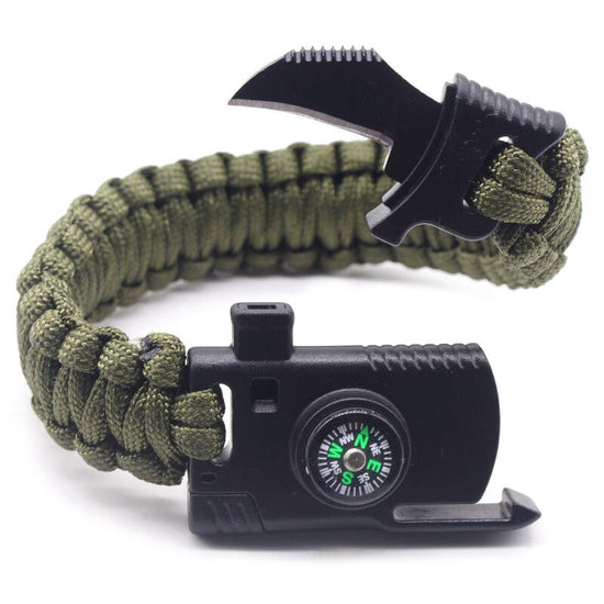 A black braided paracord survival bracelet is shown partially unbuckled, revealing a small knife blade, a compass on the buckle, and the ridged edge of a fire starter.