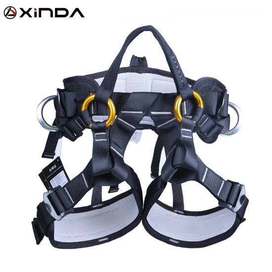 A XINDA half-body climbing harness with black webbing, white padding on the waist and thigh loops, orange gear loops, and silver metal D-rings is shown against a white background. The XINDA logo is visible at the top.