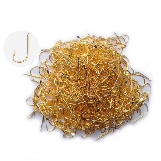 A pile of approximately 100 small, golden-colored fly fishing hooks with barbs, and a close-up inset of a single hook showing its shape.
