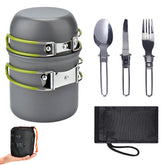 A compact grey camping cookware set is shown disassembled against a white background. It includes a pot with a lid and folding green handles, a smaller bowl with folding green handles, a folding spoon, a folding knife, a folding fork, and a black mesh storage bag. A hand is shown holding the packed set in its mesh bag.