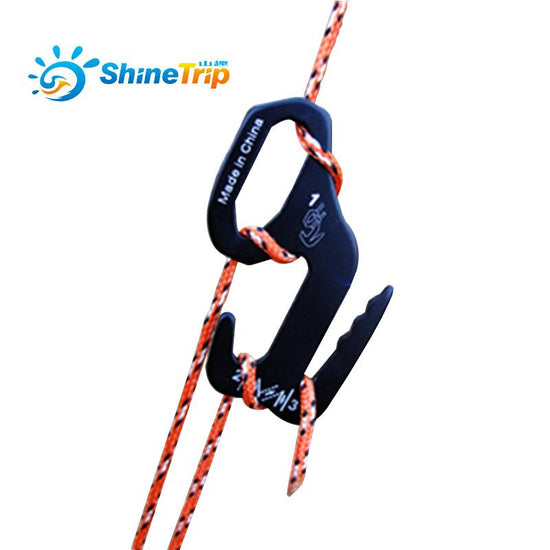 A black ShineTrip aluminum alloy 9-shape buckle is shown attached to an orange and white braided rope against a blurred outdoor background. The buckle is wrapped around the rope in a way that allows for tension adjustment. The ShineTrip logo is visible in the upper left.