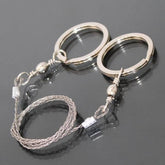 A coiled stainless steel wire saw with two silver ring handles is shown against a dark, reflective surface.