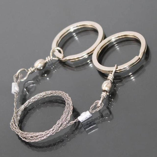 A coiled stainless steel wire saw with two silver ring handles is shown against a dark, reflective surface.
