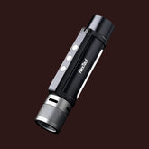 A black and silver NEXTOOL 6-in-1 flashlight is shown diagonally against a dark brown background. The flashlight has a textured silver head, a black body with the "NexTool" logo printed in white, three white indicator lights, and a lanyard attachment point at the base.