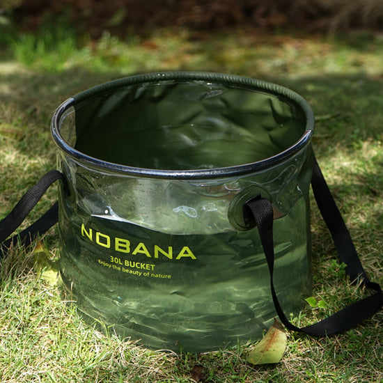  A translucent army green Nobana 30L folding bucket filled with water sits on green grass. The bucket has black trim and black carrying straps. The Nobana logo and "30L BUCKET Enjoy the beauty of nature" are printed in yellow on the side.