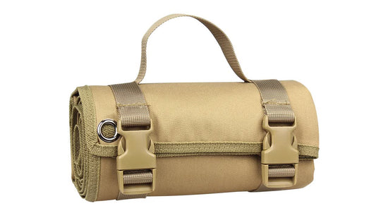 A rolled-up tactical mat with a camouflage pattern (greens, browns, and tans) is shown secured with two tan nylon straps and brown plastic buckles against a white background. A tan carrying handle extends from the top of the rolled mat.