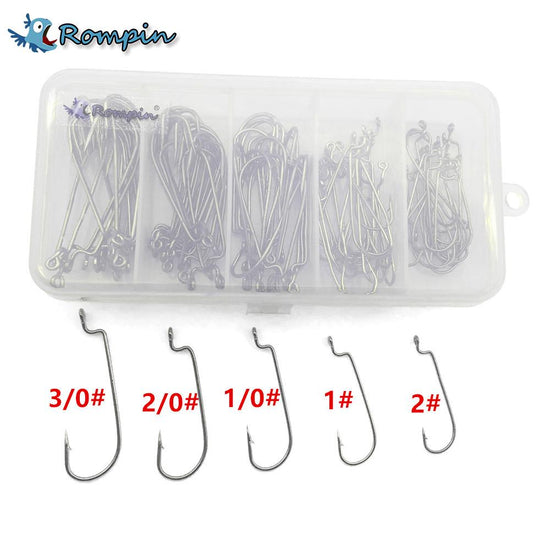 A clear plastic box containing approximately 100 silver jig head fishing hooks of various sizes, organized into five compartments. Below the box are individual hooks labeled with sizes 3/0