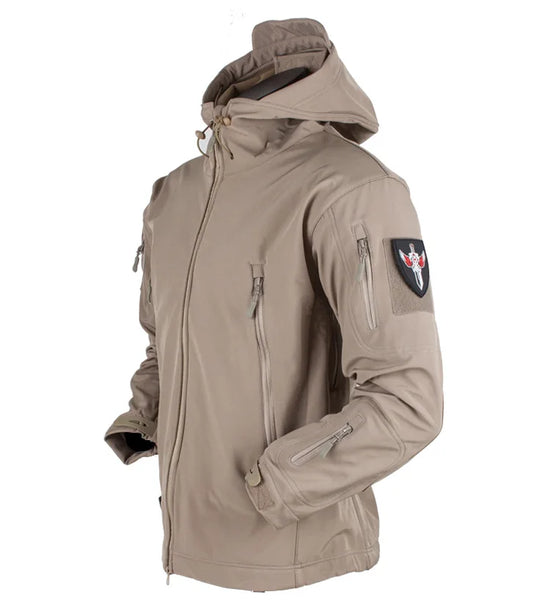 A tan-colored army-style tactical jacket with a hood, a front zipper, zippered chest and sleeve pockets, and a Velcro patch on the left sleeve.